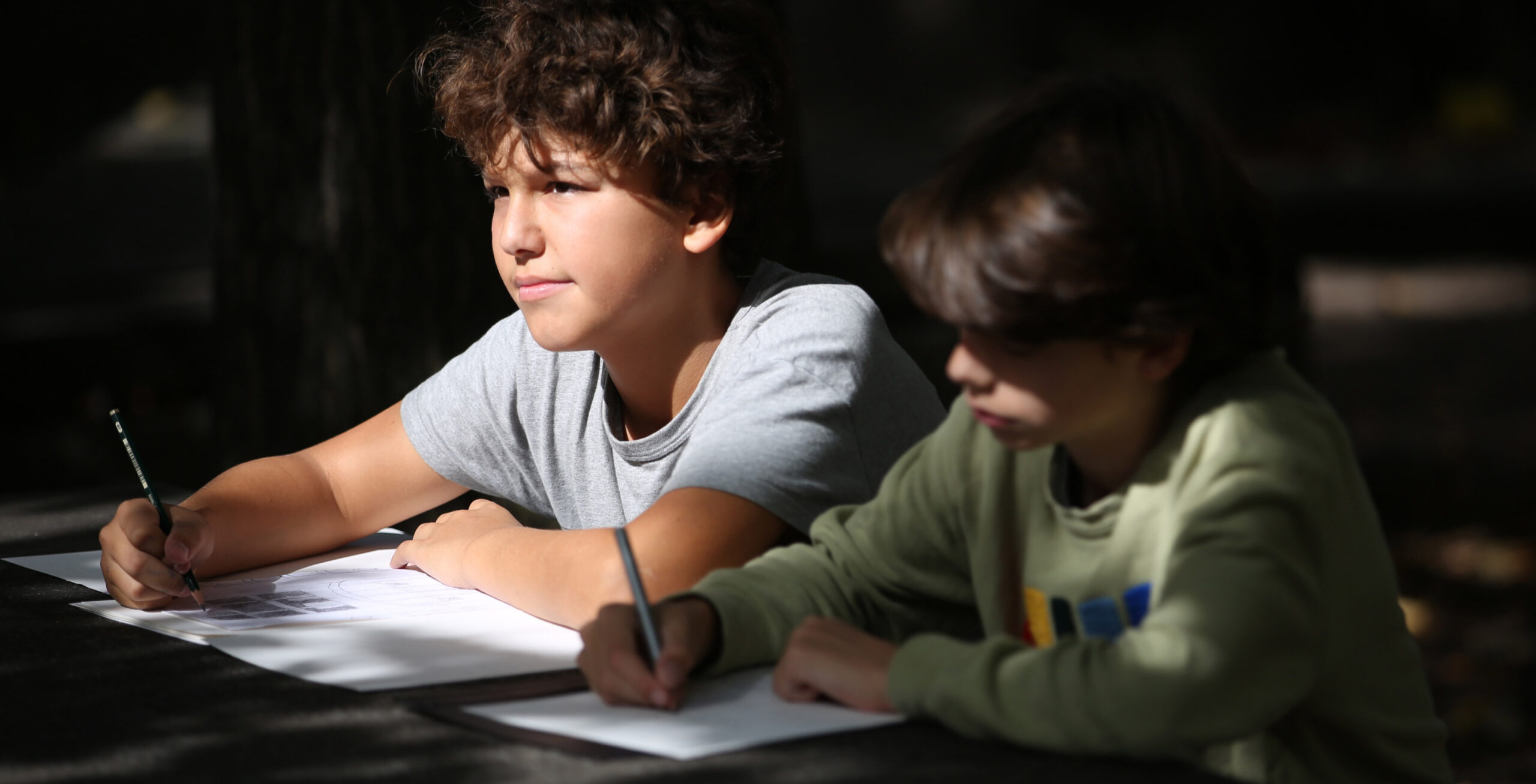 Zwei Kinder sitzen am Schultisch und schreiben etwas auf.